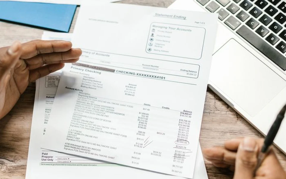 Hands reviewing a bank statement beside a laptop; illustrative stock photograph, not Formativelabz people or facilities