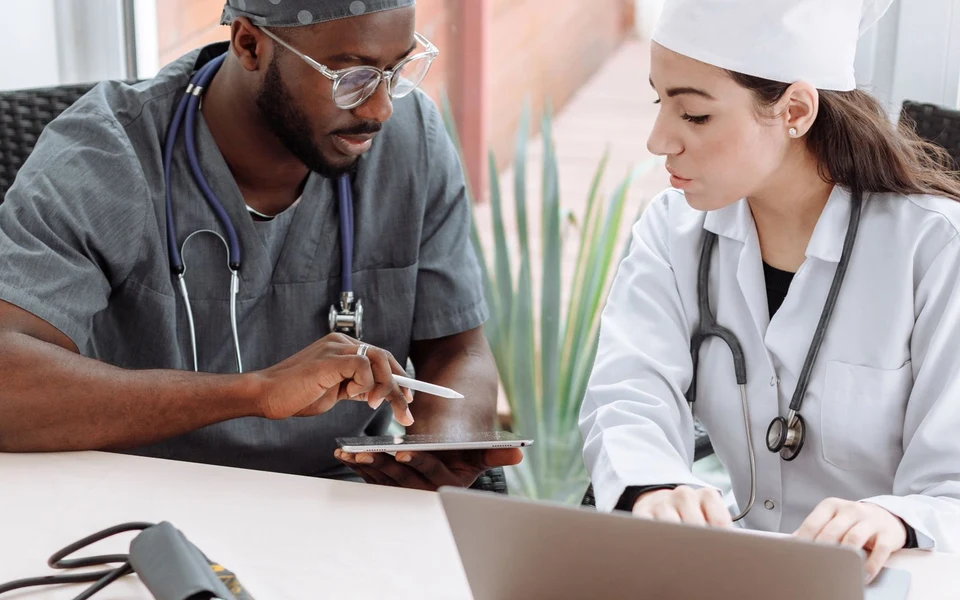 Two healthcare professionals reviewing a tablet and laptop; illustrative stock photograph, not Formativelabz people or facilities